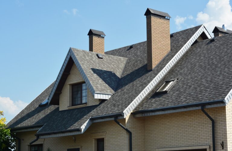 Residential home with a steep asphalt shingle roof, multiple chimneys, dormers, and skylights.