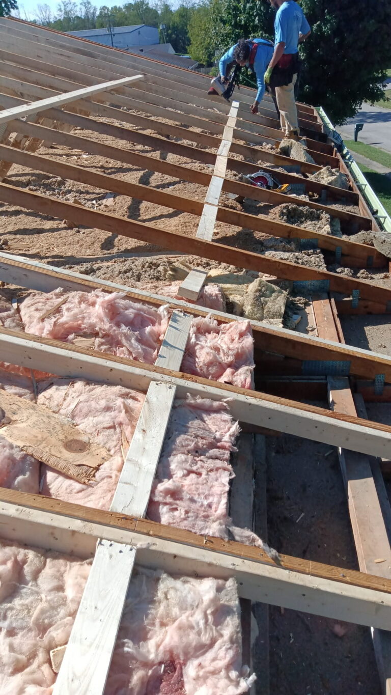 Roofers replacing roof decking and insulation during a roof installation.